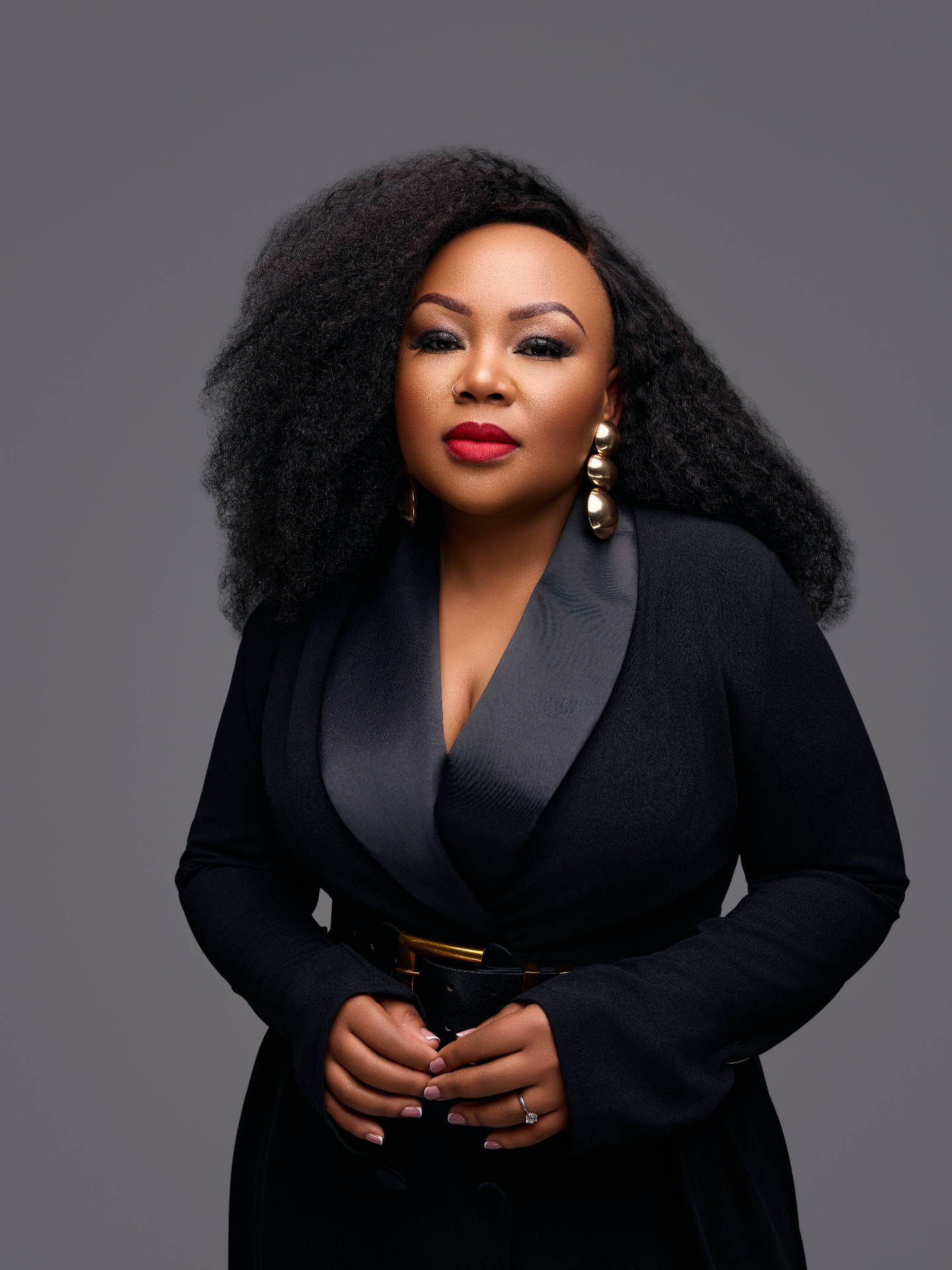 Lebo Thabethe in a black tailored coat with gold belt